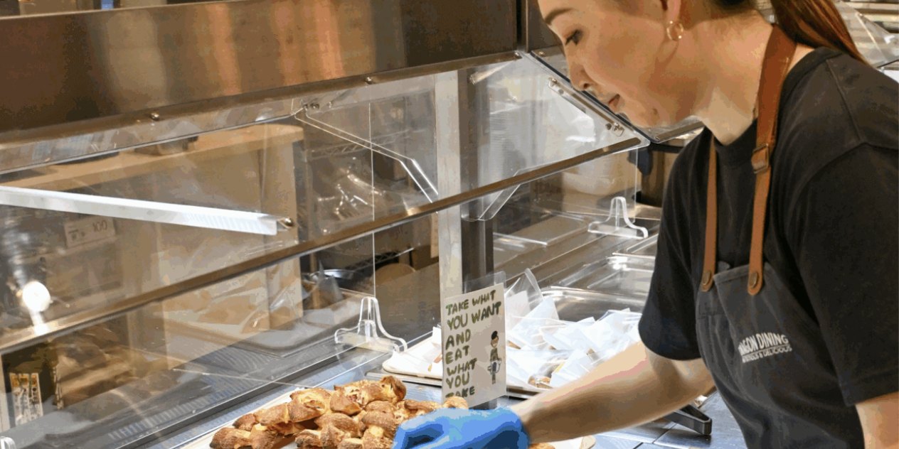 A Dragon Dining team member setting out freshly baked pastries at the cafeteria servery